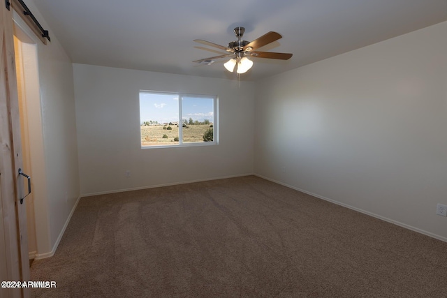 spare room with carpet, ceiling fan, and a barn door