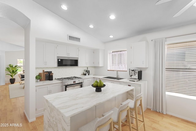 kitchen with lofted ceiling, light wood-type flooring, appliances with stainless steel finishes, and white cabinetry