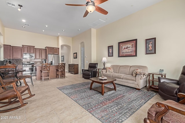 living room featuring ceiling fan, a towering ceiling, sink, and light tile patterned floors