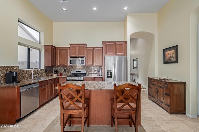 kitchen with sink, a kitchen bar, a kitchen island, stainless steel appliances, and stone countertops