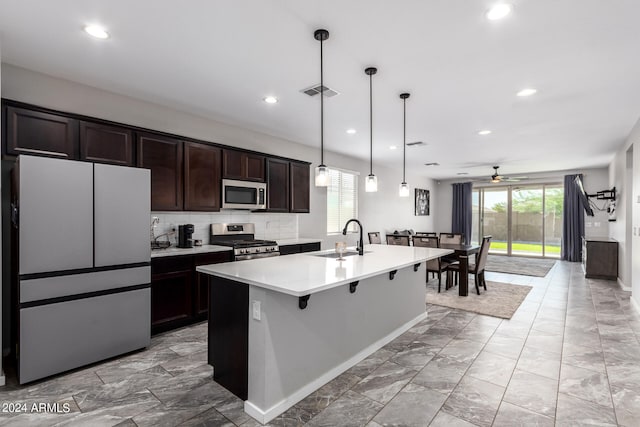 kitchen featuring a breakfast bar, a kitchen island with sink, sink, hanging light fixtures, and appliances with stainless steel finishes