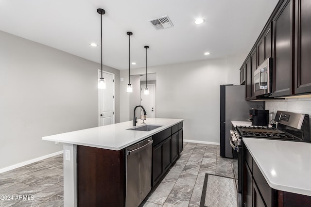 kitchen with an island with sink, sink, stainless steel appliances, and decorative light fixtures