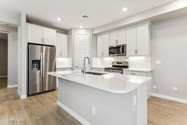 21228 N 58th St, Phoenix, AZ 85054 - kitchen featuring appliances with stainless steel finishes, a sink, light wood-style floors, baseboards, and a center island with sink