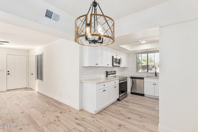 kitchen featuring light wood-type flooring, white cabinetry, pendant lighting, and appliances with stainless steel finishes