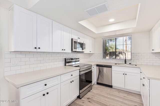 kitchen featuring light wood-type flooring, appliances with stainless steel finishes, a raised ceiling, sink, and white cabinets