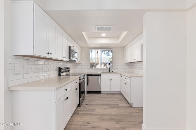 kitchen with light hardwood / wood-style flooring, backsplash, a tray ceiling, white cabinetry, and appliances with stainless steel finishes