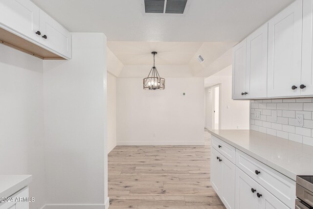 kitchen featuring white cabinetry, hanging light fixtures, decorative backsplash, light hardwood / wood-style floors, and a chandelier