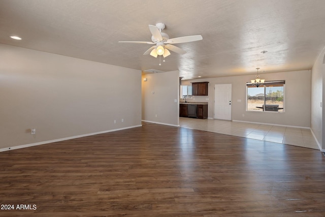 unfurnished living room featuring dark hardwood / wood-style flooring, sink, ceiling fan with notable chandelier, and a textured ceiling