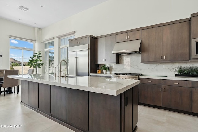 20475 E Indiana Ave, Queen Creek, AZ 85142 - kitchen featuring under cabinet range hood, appliances with stainless steel finishes, a sink, backsplash, and a kitchen island with sink