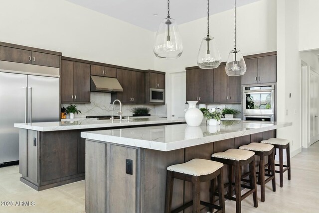 20475 E Indiana Ave, Queen Creek, AZ 85142 - kitchen with a large island, under cabinet range hood, built in appliances, dark brown cabinets, and a high ceiling