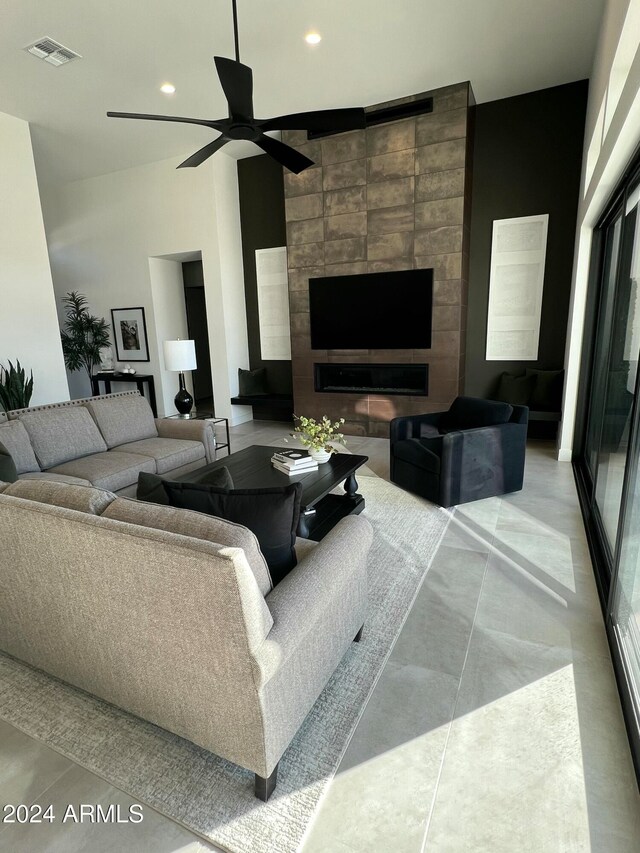 living room featuring ceiling fan, a towering ceiling, and a tile fireplace