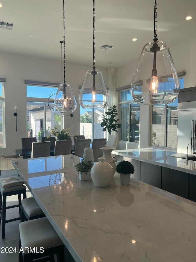 kitchen featuring decorative light fixtures, light stone counters, stainless steel built in refrigerator, and an inviting chandelier