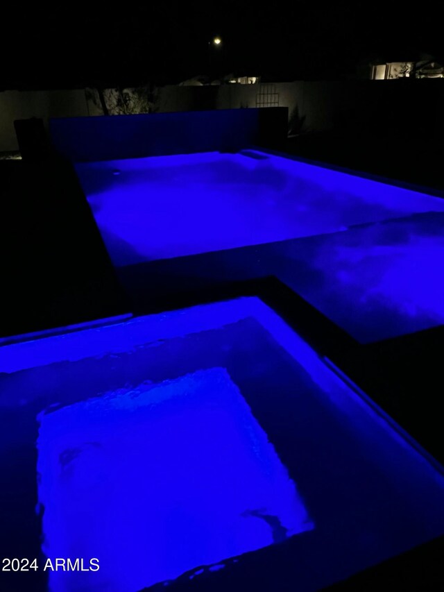 pool at night featuring an in ground hot tub