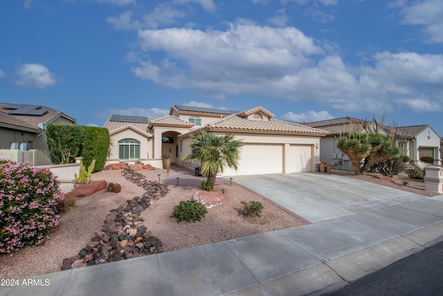 mediterranean / spanish house featuring solar panels, an attached garage, a tile roof, stucco siding, and driveway