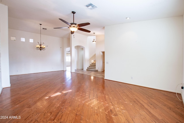 empty room featuring visible vents, light wood finished floors, arched walkways, stairs, and ceiling fan with notable chandelier