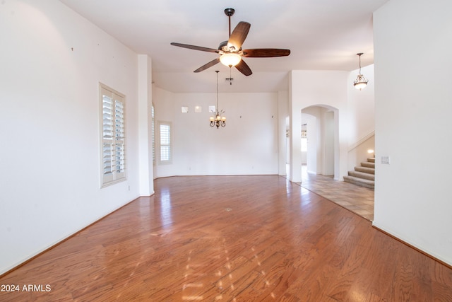 unfurnished living room featuring arched walkways, ceiling fan with notable chandelier, stairs, and wood finished floors