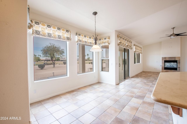 unfurnished dining area with light tile patterned floors, a tile fireplace, ceiling fan, and vaulted ceiling