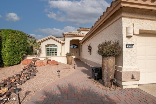 view of exterior entry featuring a tiled roof, an attached garage, and stucco siding