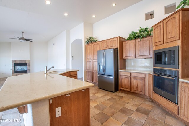 kitchen featuring a ceiling fan, a tiled fireplace, a sink, stainless steel appliances, and arched walkways