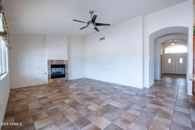 unfurnished living room with arched walkways, visible vents, a tile fireplace, and a ceiling fan