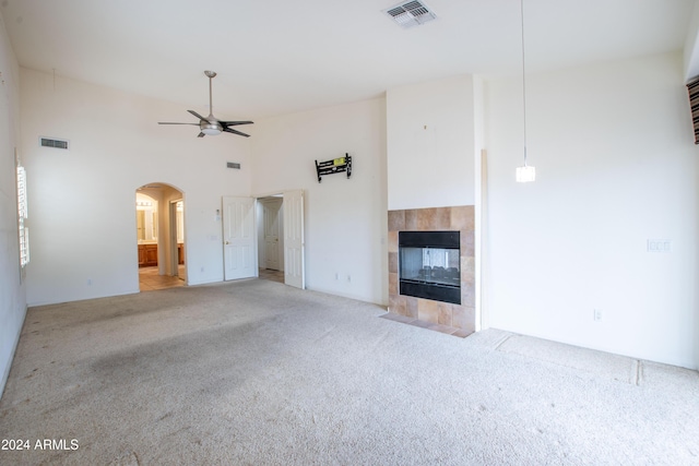 unfurnished living room with visible vents, carpet floors, a tile fireplace, arched walkways, and a ceiling fan