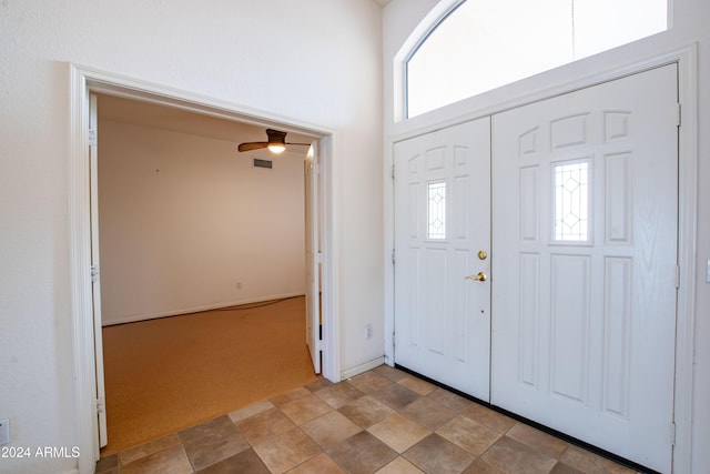 carpeted entryway with ceiling fan, visible vents, baseboards, and a towering ceiling