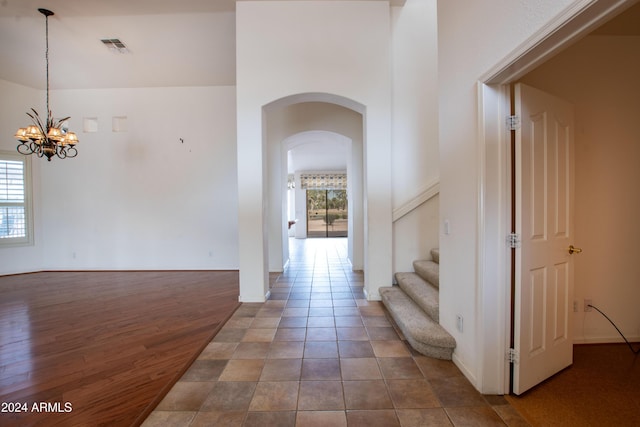 corridor with a wealth of natural light, visible vents, a notable chandelier, and wood finished floors