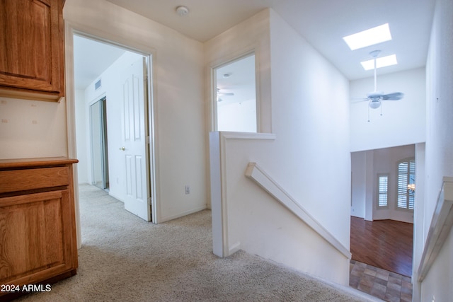 corridor featuring an upstairs landing, visible vents, light colored carpet, and a skylight