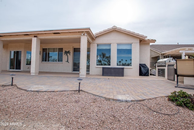 rear view of house with stucco siding, a patio, and exterior kitchen