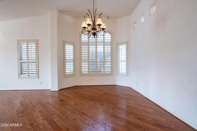 empty room featuring a chandelier, visible vents, a healthy amount of sunlight, and wood finished floors