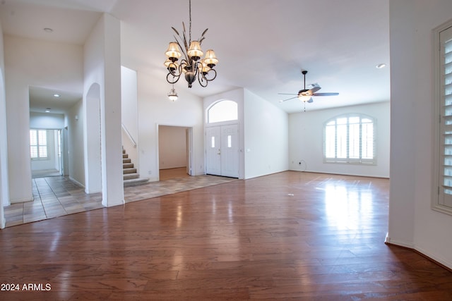 foyer entrance featuring ceiling fan with notable chandelier, stairs, a high ceiling, and wood finished floors