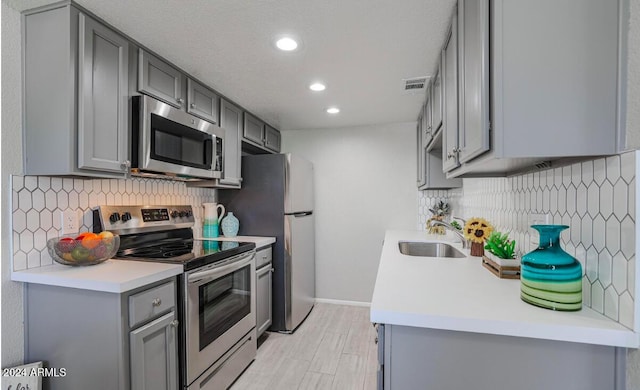 kitchen with stainless steel appliances, gray cabinets, light countertops, visible vents, and a sink