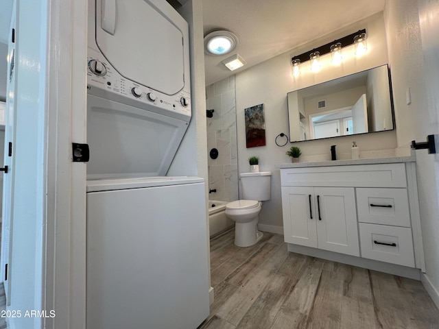 bathroom with vanity, a shower, stacked washer and clothes dryer, hardwood / wood-style floors, and toilet