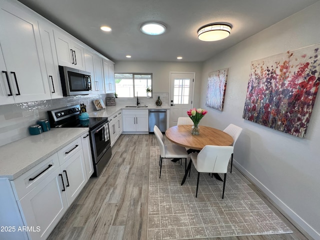 kitchen with backsplash, sink, light hardwood / wood-style flooring, appliances with stainless steel finishes, and white cabinetry