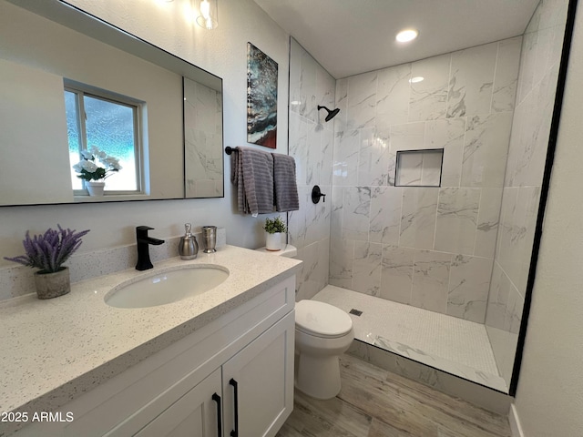 bathroom with hardwood / wood-style flooring, vanity, toilet, and a tile shower