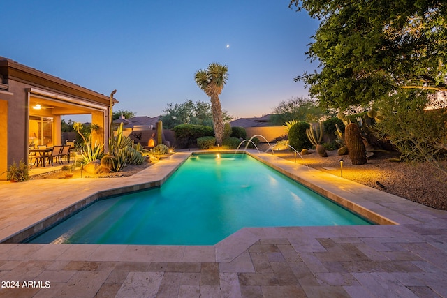 pool at dusk with pool water feature and a patio area