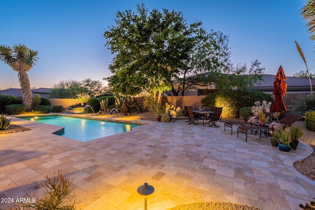 pool at dusk featuring pool water feature and a patio area