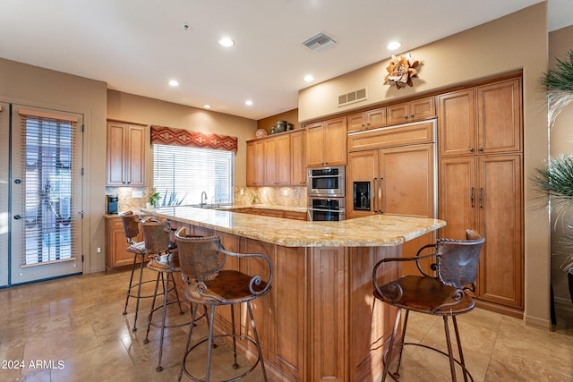 kitchen with sink, backsplash, a spacious island, a breakfast bar area, and light stone countertops