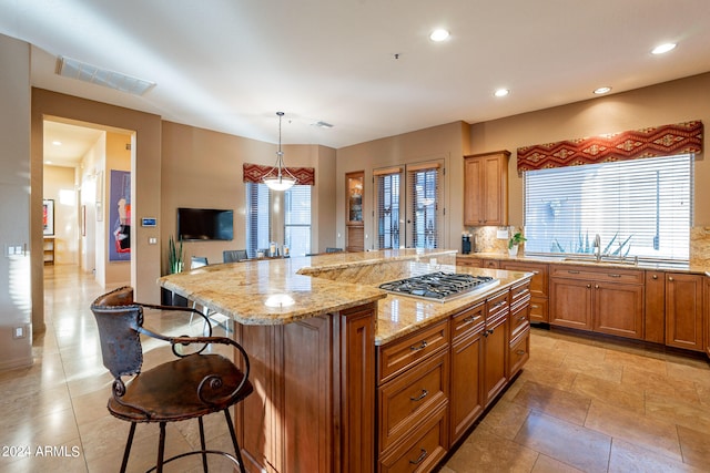 kitchen featuring light stone counters, pendant lighting, a kitchen island, stainless steel gas cooktop, and a kitchen breakfast bar