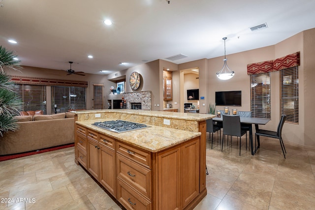 kitchen featuring a tile fireplace, a kitchen island, pendant lighting, ceiling fan, and stainless steel gas stovetop