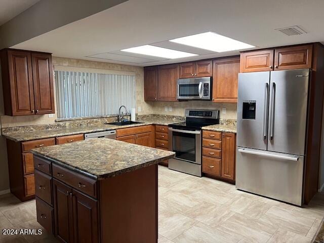 kitchen featuring a kitchen island, light stone countertops, appliances with stainless steel finishes, and sink