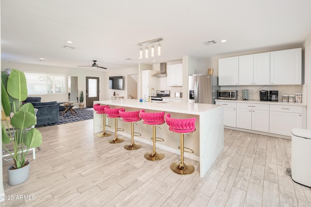 kitchen featuring white cabinets, stainless steel appliances, wall chimney exhaust hood, and a spacious island