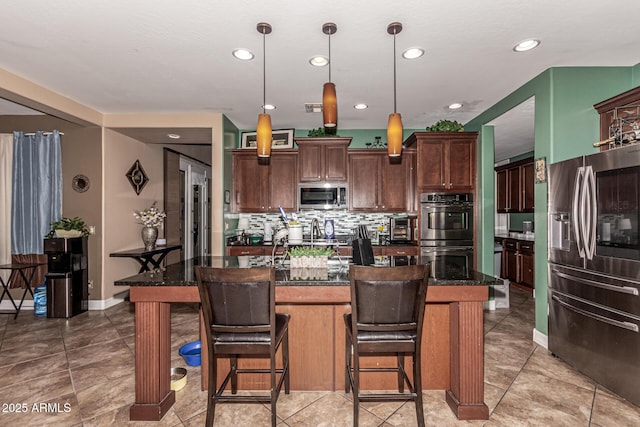 kitchen featuring appliances with stainless steel finishes, dark brown cabinetry, a kitchen island, hanging light fixtures, and a breakfast bar area