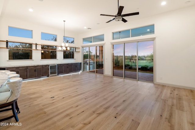 living room with wine cooler, a towering ceiling, ceiling fan with notable chandelier, and light wood-type flooring