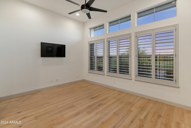 spare room featuring a towering ceiling, light wood-type flooring, and ceiling fan