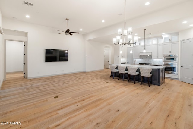 kitchen with white cabinetry, hanging light fixtures, stainless steel appliances, a center island with sink, and light wood-type flooring