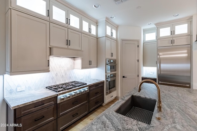 kitchen featuring light stone countertops, sink, stainless steel appliances, tasteful backsplash, and dark brown cabinets