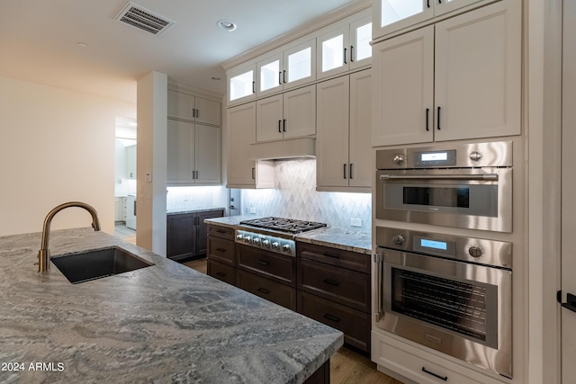 kitchen with light stone countertops, sink, dark brown cabinets, white cabinets, and appliances with stainless steel finishes