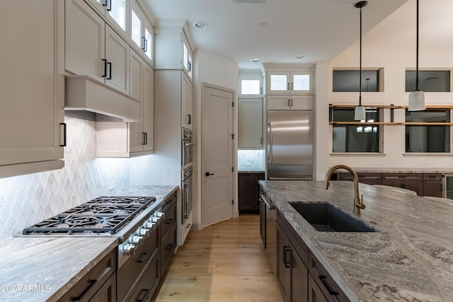 kitchen featuring sink, stainless steel appliances, light stone counters, light hardwood / wood-style floors, and decorative light fixtures