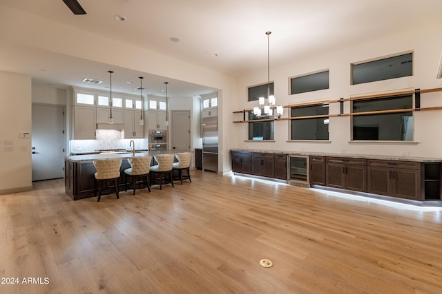 kitchen featuring hanging light fixtures, stainless steel appliances, wine cooler, light hardwood / wood-style flooring, and a notable chandelier